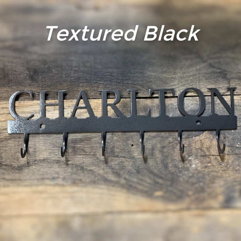 Puede incluir: Llavero de metal negro texturizado con el nombre "CHARLTON" recortado. El llavero tiene cinco ganchos debajo del nombre. El texto "Textured Black" est&aacute; encima del nombre. El llavero est&aacute; montado sobre una superficie de madera.