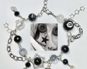 May include: A silver chain bracelet with black and white beads, a silver star charm, a silver heart charm, and a black and white 8-ball charm. The bracelet also features a small silver chain with stars.