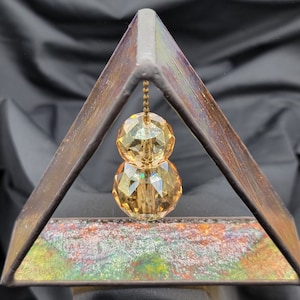 May include: A triangular metal frame with a stained glass design, featuring a hanging crystal prism with two amber-coloured facets.