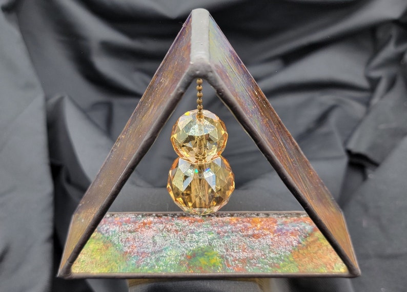 May include: A triangular metal frame with a stained glass design, featuring a hanging crystal prism with two amber-coloured facets.
