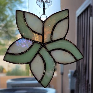 K&ouml;nnte beinhalten: Ein Buntglas-Sonnenf&auml;nger in Form einer Blume mit gr&uuml;nen und wei&szlig;en Glasscheiben und schwarzem Metallrahmen.