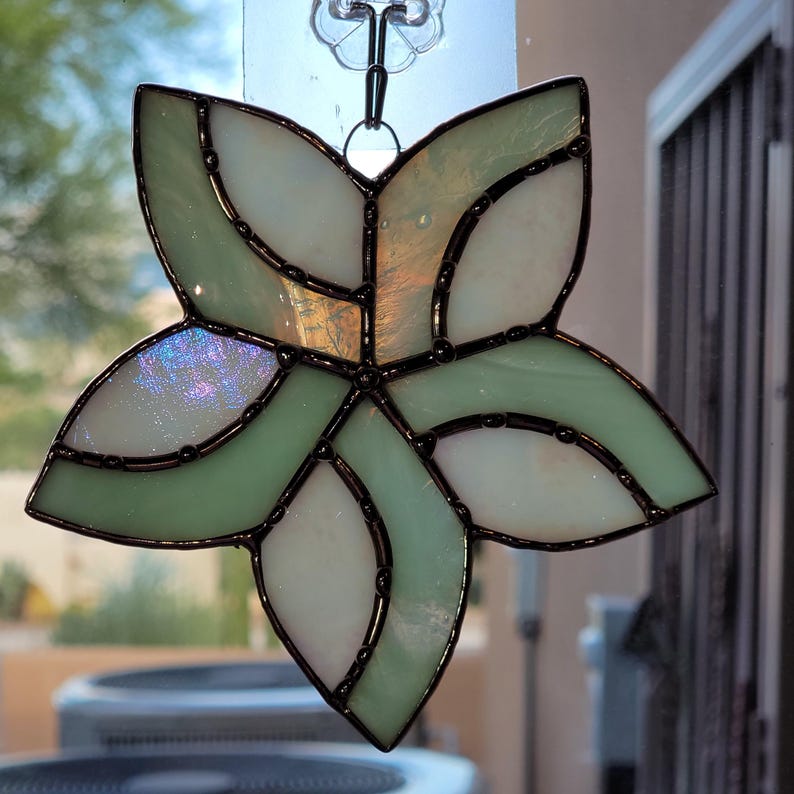 K&ouml;nnte beinhalten: Ein Buntglas-Sonnenf&auml;nger in Form einer Blume mit gr&uuml;nen und wei&szlig;en Glasscheiben und schwarzem Metallrahmen.