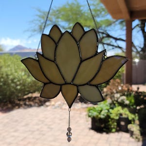Peut inclure: Un attrape-soleil en forme de fleur de lotus en vitrail, suspendu par une cha&icirc;ne. Les p&eacute;tales jaunes sont soulign&eacute;s de noir. Un petit charme de perles est suspendu en dessous. Fond bleu et verdure.