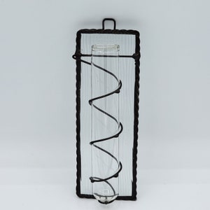 Peut inclure: Un cadre en m&eacute;tal noir avec un tube en verre transparent &agrave; l'int&eacute;rieur. Le tube est maintenu en place par un fil noir qui s'enroule autour de lui. Le cadre est mont&eacute; sur un mur blanc.