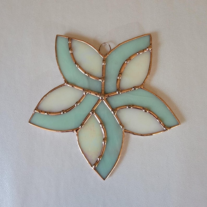 K&ouml;nnte beinhalten: Ein Buntglas-Sonnenf&auml;nger in Form einer Blume mit sechs Bl&uuml;tenbl&auml;ttern. Die Blume besteht aus hellblauem und wei&szlig;em Glas mit Kupferfolien-Akzenten.