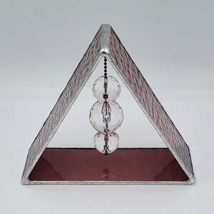 May include: A pink stained glass triangle with a silver frame and three clear crystal beads hanging from a chain inside.