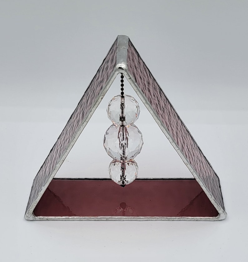 May include: A pink stained glass triangle with a silver frame and three clear crystal beads hanging from a chain inside.