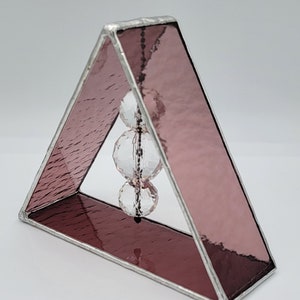 May include: A small triangular stained glass sculpture with a pink iridescent finish. Three clear crystal beads hang from the top of the triangle.