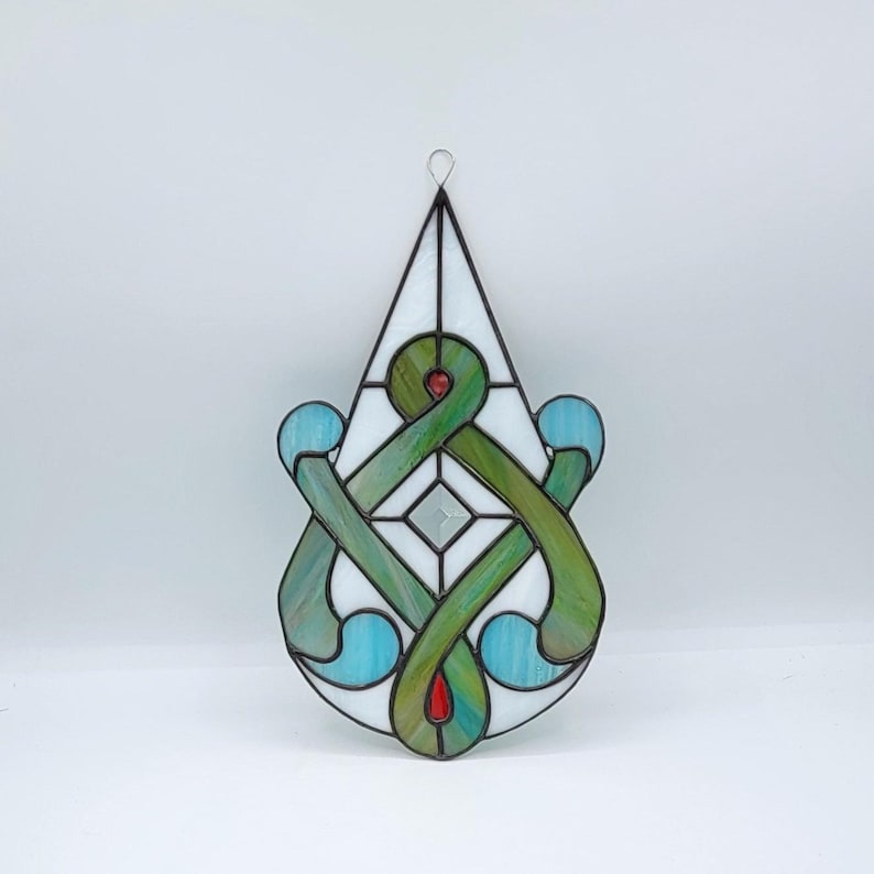 May include: A stained glass window hanging ornament with a teardrop shape. The ornament features a green and blue design with a white center.