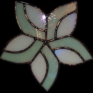 K&ouml;nnte beinhalten: Eine hellgr&uuml;ne Glasbl&uuml;te mit wei&szlig;em Zentrum. Die Bl&uuml;te hat ein wirbelndes Design und ist mit Schwarz umrandet.