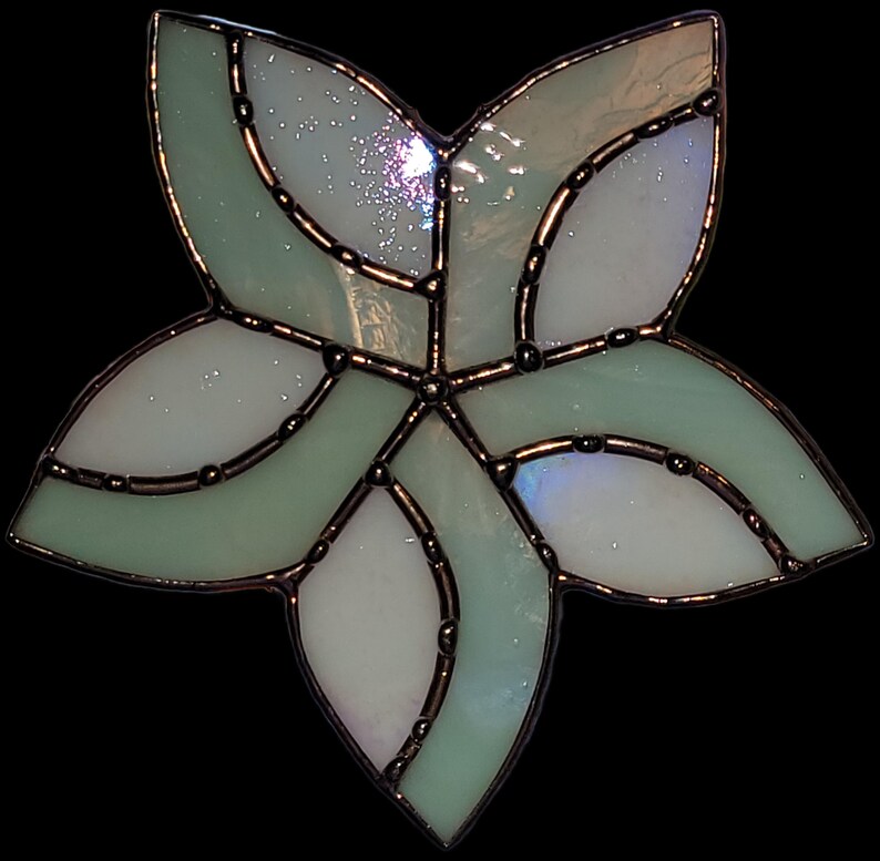 K&ouml;nnte beinhalten: Eine hellgr&uuml;ne Glasbl&uuml;te mit wei&szlig;em Zentrum. Die Bl&uuml;te hat ein wirbelndes Design und ist mit Schwarz umrandet.