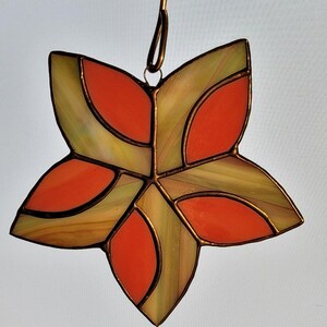 K&ouml;nnte beinhalten: Ein Ornament aus Buntglas in Form eines Sterns mit geometrischem Muster. Der Stern besteht aus orangem und gr&uuml;nem Glas und hat einen Aufh&auml;nger aus Kupferdraht.