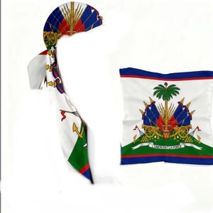 May include: Two items featuring the Haitian flag: a headscarf and a square scarf. The headscarf is white with red, blue, and gold accents, and a long tail. The square scarf has a white background with the Haitian coat of arms and a blue, red, and green border.