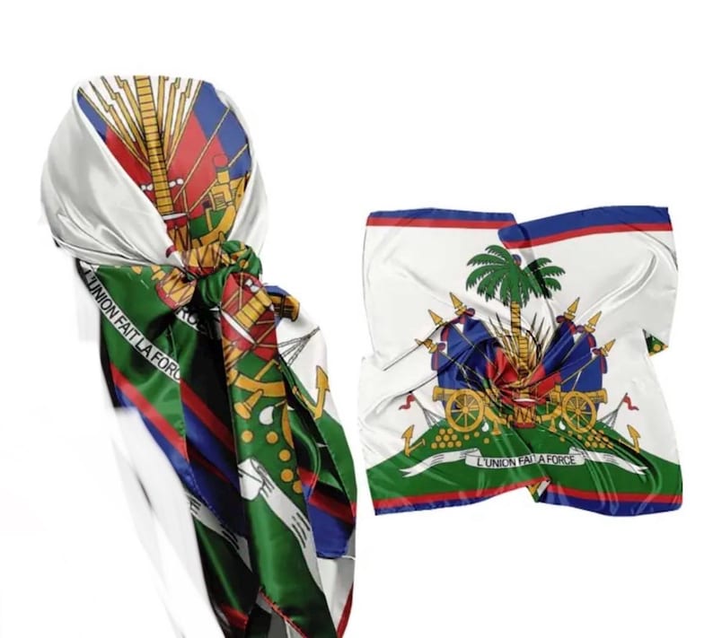 May include: Two silk scarves featuring the Haitian coat of arms. One scarf is knotted, displaying the colors of the Haitian flag: red, blue, green, and white. The other scarf is unfolded, showing the emblem with the text "L'UNION FAIT LA FORCE."
