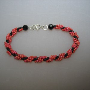 May include: A black and coral beaded bracelet with silver clasps. The bracelet is made with small beads and has a twisted design.