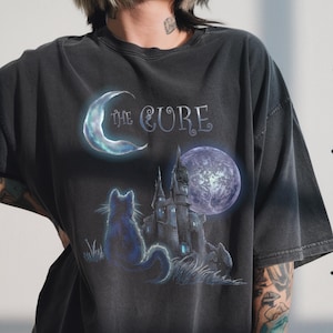 Dark grey tshirt featuring gothic text The Cure with a silhouette black cat sitting in front of a dark castle and full moon.