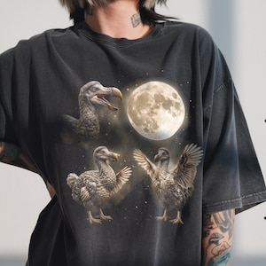 Könnte beinhalten: Dunkelgraues T-Shirt mit einer Grafik von drei Dodos und einem Vollmond. Die Dodos sind in verschiedenen Posen dargestellt, wobei einer zu schreien scheint. Das Design hat einen Vintage-Look.