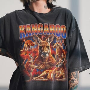 May include: Dark gray t-shirt featuring a graphic of several kangaroos with a red, orange, and blue background and lightning bolts. The word "KANGAROO" is printed across the top in a gradient font.