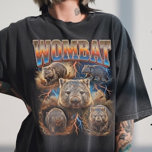 May include: Dark gray t-shirt featuring a graphic of several wombats with lightning bolts and the word "WOMBAT" in a colorful, stylized font. The design has a vintage, distressed look.