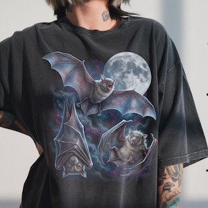 May include: Dark grey t-shirt with a detailed illustration of three bats in flight against a full moon and a starry nebula. The bats are depicted with realistic fur and wings, creating a gothic aesthetic.