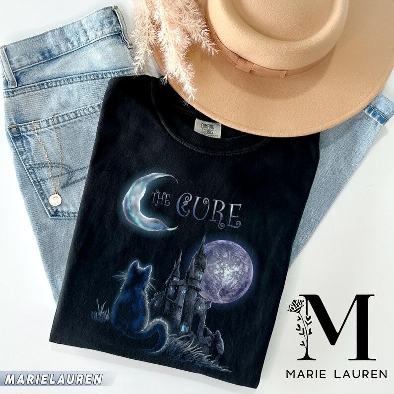 Dark grey tshirt featuring gothic text The Cure with a silhouette black cat sitting in front of a dark castle and full moon.
