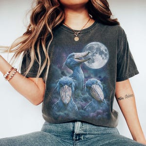 Vintage style three shoebill storks moon graphic printed on dark washed t-shirt, scary dinosaur bird galaxy design.