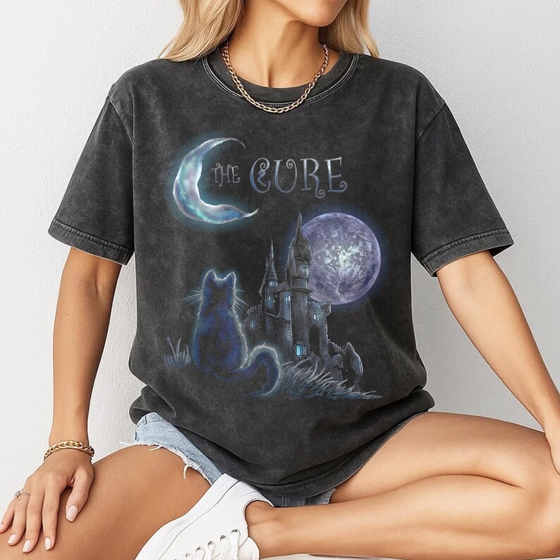 Dark grey tshirt featuring gothic text The Cure with a silhouette black cat sitting in front of a dark castle and full moon.