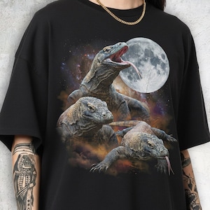 May include: Black t-shirt featuring a graphic of three Komodo dragons with a full moon in the background. The dragons are detailed with open mouths and long tongues. The design is set against a starry sky.