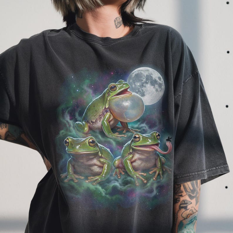 Three realistic green frogs positioned under a large luminous full moon. The top frog has an inflated translucent vocal sac as if croaking. Below, one frog faces forward with a calm expression, while the other sticks its long tongue out to catch a fly. Cosmic teal and purple nebula mist with stars in a retro 90s galaxy style.