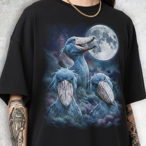 Vintage style three shoebill storks moon graphic printed on dark washed t-shirt, scary dinosaur bird galaxy design.