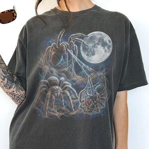 Vintage style three tarantulas moon graphic printed on dark washed t-shirt, hairy spider galaxy design spinning web.