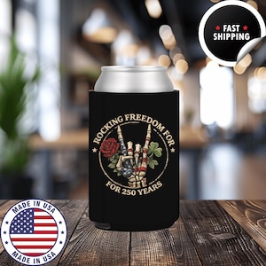 May include: Black can cooler with the text "Rocking Freedom For 250 Years." The design includes a hand gesture with the American flag, a red rose, and a shamrock. A "Made in USA" sticker is visible.