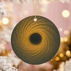 May include: A round Christmas ornament with a binary code design. The ornament features a swirling pattern of gold numbers on a dark background, with a central black hole effect. It hangs from a gold string.