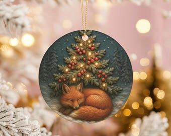 Peut inclure: Ornement de Noël rond représentant un renard endormi sous un sapin décoré. L'ornement a un fond bleu foncé et une ficelle dorée pour l'accrocher. Le renard est orange et l'arbre est vert avec des baies rouges.