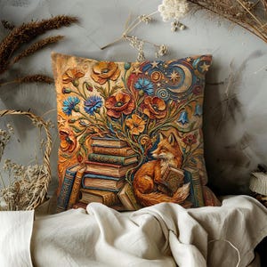 May include: Square throw pillow with a whimsical design. The pillow features a stack of books, vibrant orange poppies, blue cornflowers, and a fox reading a book. The background includes a crescent moon, stars, and a textured, aged appearance.