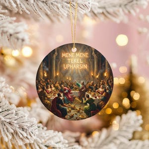 May include: Round Christmas ornament featuring a religious scene with many figures gathered around a table. The text "MENE MENE TEKEL UPHARSIN" is displayed in gold lettering. The ornament has a gold string for hanging.