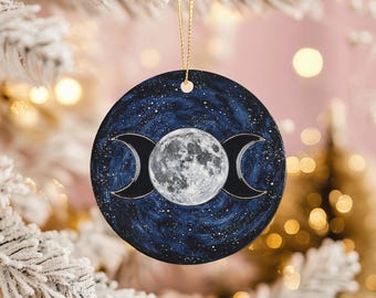 May include: Round ceramic ornament featuring a celestial design. The ornament has a dark blue background with a full moon in the center, flanked by two crescent moons. The design includes white stars and a gold string for hanging.