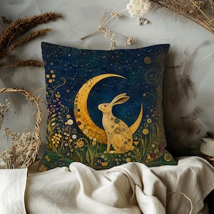 May include: A square throw pillow featuring a dark blue starry night sky background with a large golden crescent moon and a golden rabbit sitting in a field of yellow flowers and swirling botanical patterns, creating a celestial and nature-inspired design.