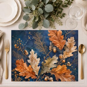 May include: A rectangular placemat featuring a deep navy blue background with a printed design of golden brown oak leaves, delicate twigs, and small acorns. The artwork displays a mix of detailed leaf textures and scattered gold paint splatters.