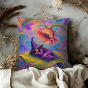 May include: A square throw pillow featuring a colorful illustration of a figure in a purple robe and pointed hat sleeping on a large green leaf. Above the figure, a large pink flower blooms against a swirling background of purple, blue, and gold.