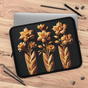 Pode incluir: Capa preta para laptop com um design floral. Apresenta flores e folhas amarelo-dourado dispostas em três buquês, cada um emergindo de uma base em forma de baguete. O fundo é preto.