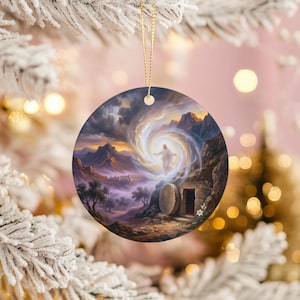 May include: Round Christmas ornament featuring a religious scene. The artwork depicts a figure in white emerging from a bright vortex, with a tomb and landscape in the foreground. The ornament has a gold string for hanging.