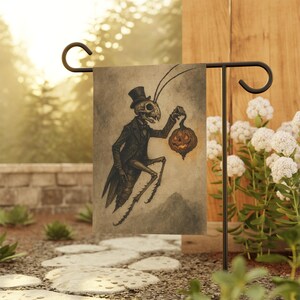 May include: A Halloween garden flag features a skeletal insect figure in a black suit and top hat, holding a carved pumpkin lantern. The flag is displayed on a black metal stand, with a blurred outdoor background.