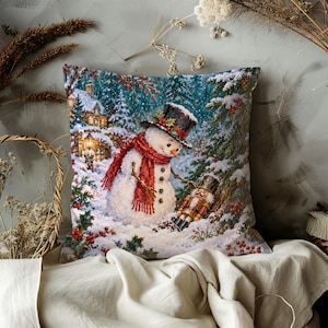 May include: A square throw pillow featuring a printed winter scene of a snowman wearing a black top hat and red scarf, standing in a snowy forest next to a nutcracker figurine. The background includes a lit house, pine trees, and red berries.