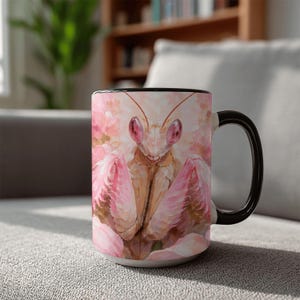 May include: A ceramic coffee mug featuring a detailed illustration of a praying mantis with pink and brown tones. The mug has a black handle and rim, and the background is a soft pink floral design. A unique and artistic gift.