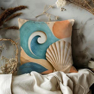 May include: A square throw pillow featuring a printed graphic of a large seashell in the foreground against a stylized coastal scene. The design includes abstract blue ocean waves, a tan sandy beach, and a circular orange sun on a cream background.