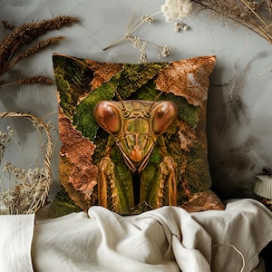 May include: Decorative square pillow featuring a detailed image of a praying mantis with large, reddish-brown eyes. The insect is set against a backdrop of green and brown leaves, creating a naturalistic design. The pillow is a unique home decor item.