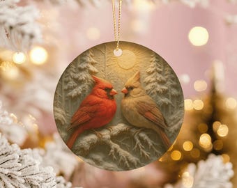 May include: Round Christmas ornament featuring two cardinals perched on a branch. The ornament has a winter scene with a red male cardinal and a tan female cardinal. The background includes snow-covered trees and a soft, warm glow.