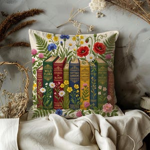 May include: A decorative square pillow featuring a colorful floral and book design. The pillow displays a row of vintage books with titles like "Wild Flora" and "Poetry of Nature," surrounded by daisies, poppies, and other flowers. The pillow is on a cream-colored background.