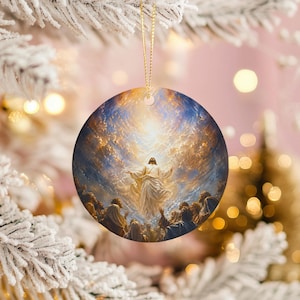 Puede incluir: Adorno navideño redondo con una escena religiosa. La obra representa una figura con túnica blanca y brazos extendidos, rodeada de luz brillante y una multitud. El adorno cuelga de un hilo dorado.